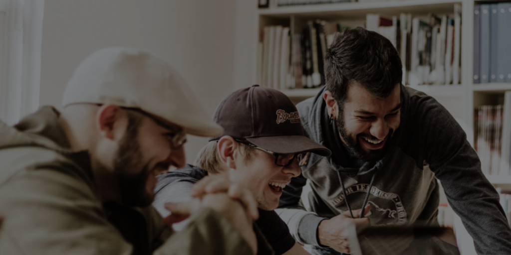 Three male colleagues joyfully engaging around Scientology methods on a computer